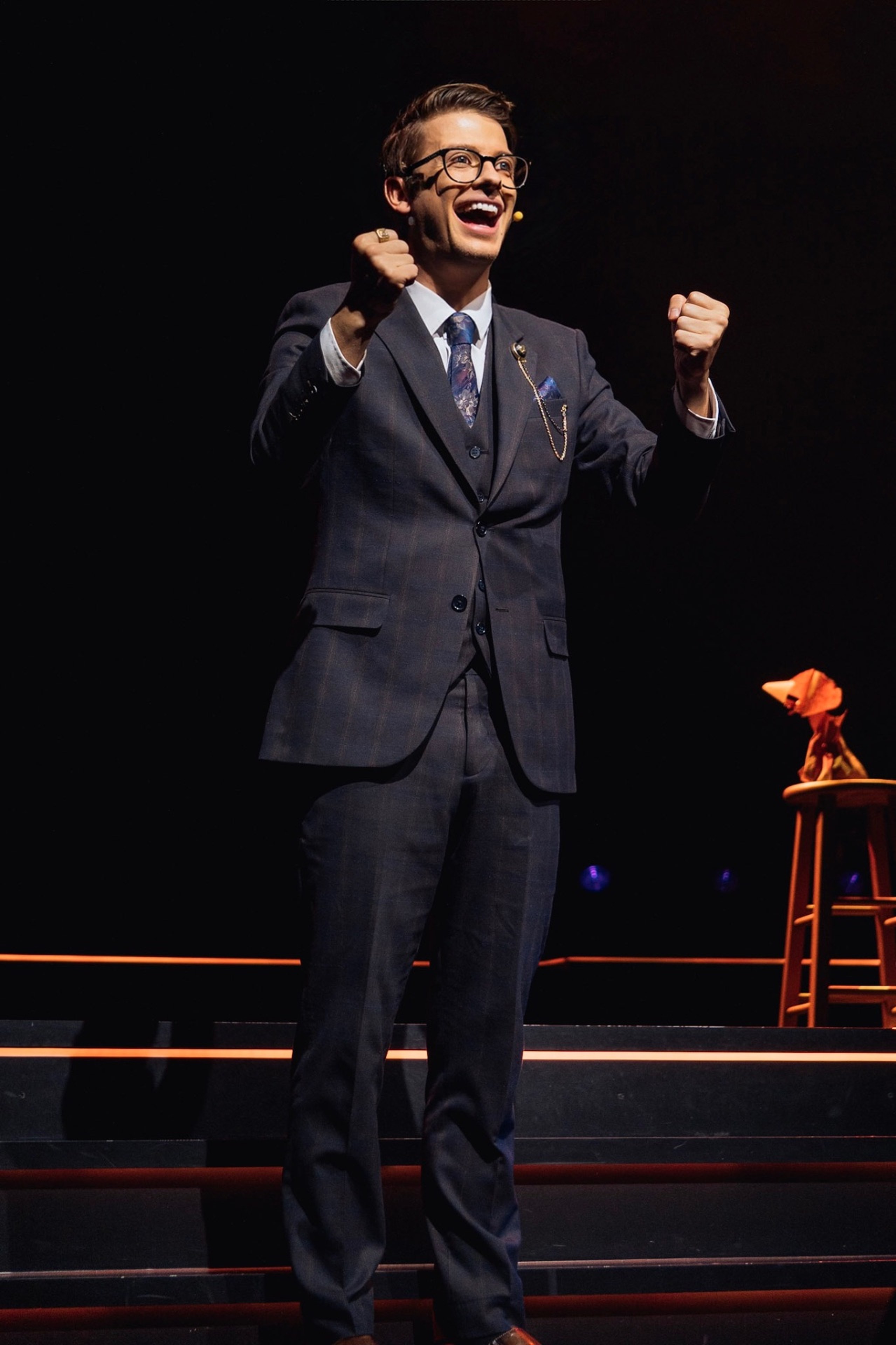 Matthew Pomeroy celebrating on a darkened theatre stage