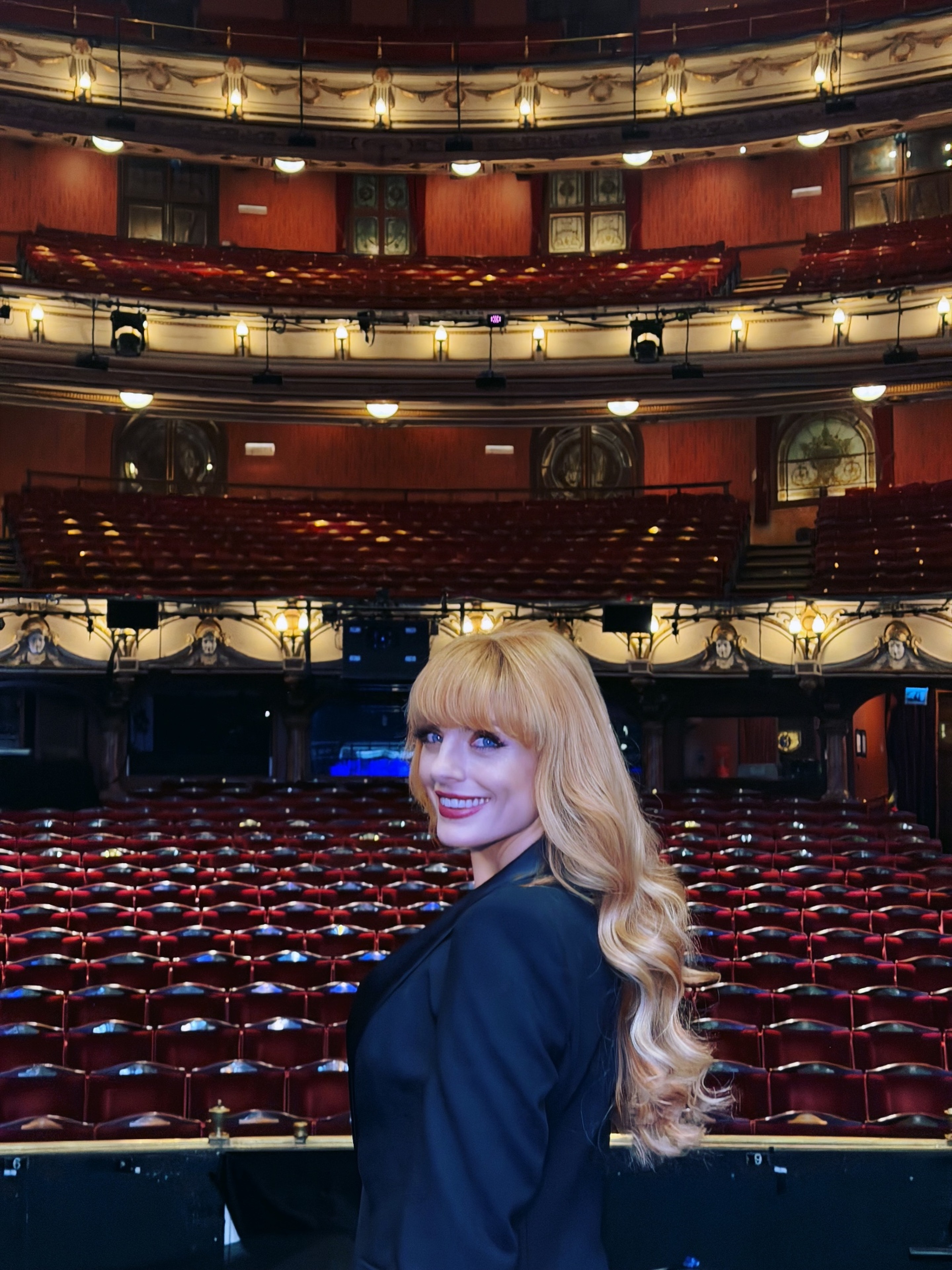 Natasha Lamb smiling in an empty grand theatre of red velvet seats
