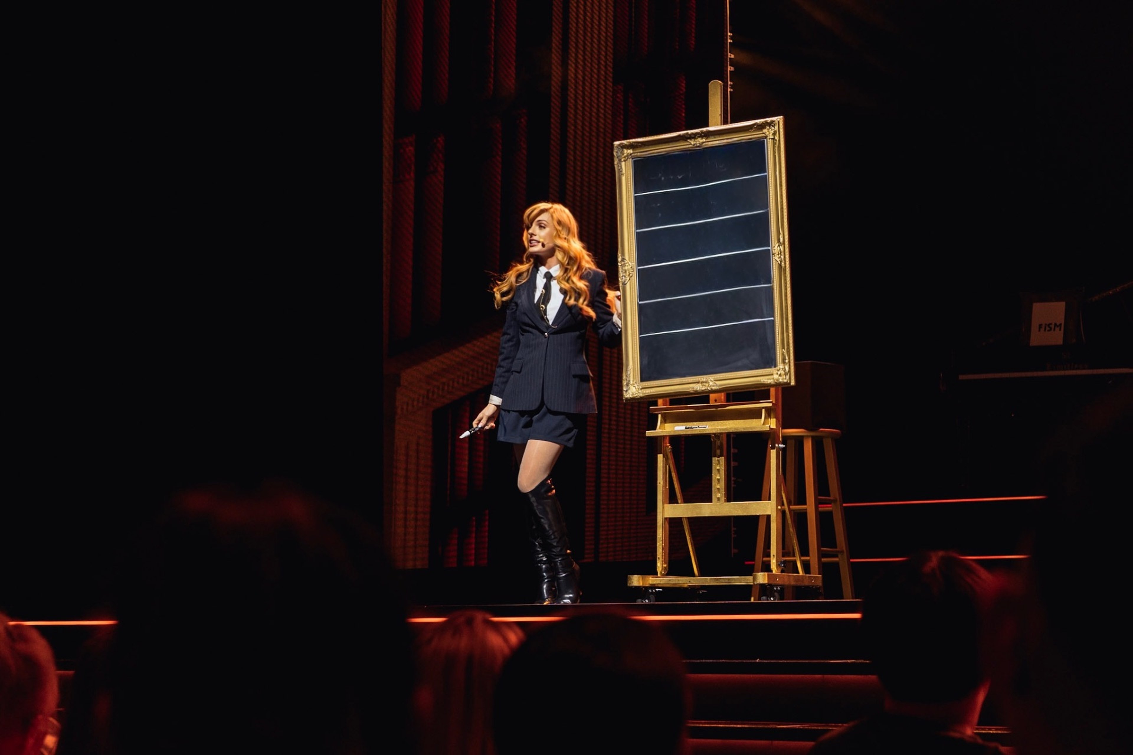Natasha Lamb presenting beside a gilded framed board on stage
