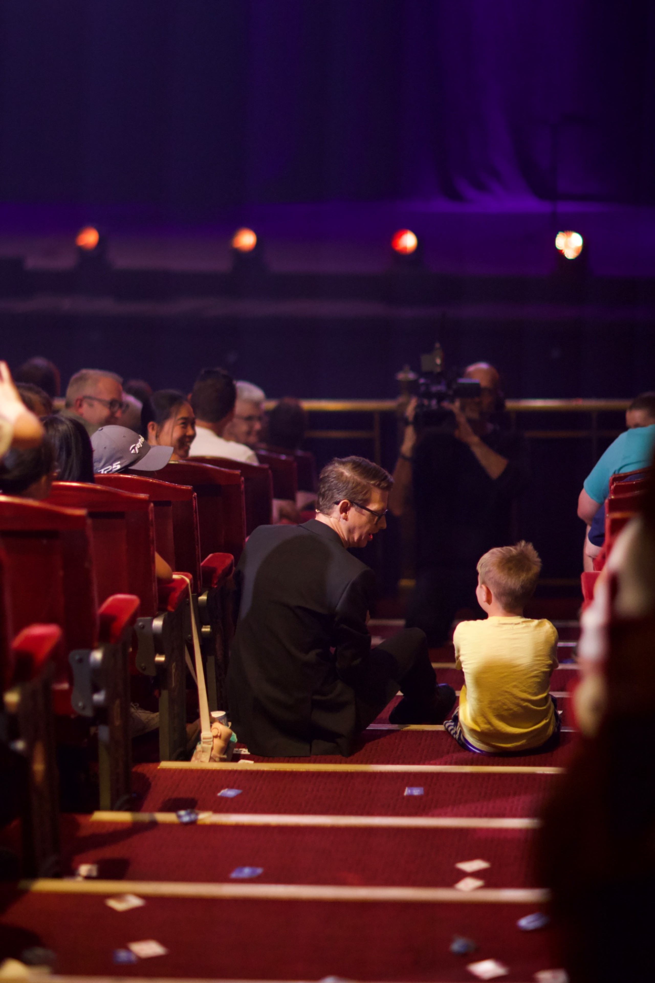 Matthew Pomeroy kneeling in the theatre aisle to talk with a young guest