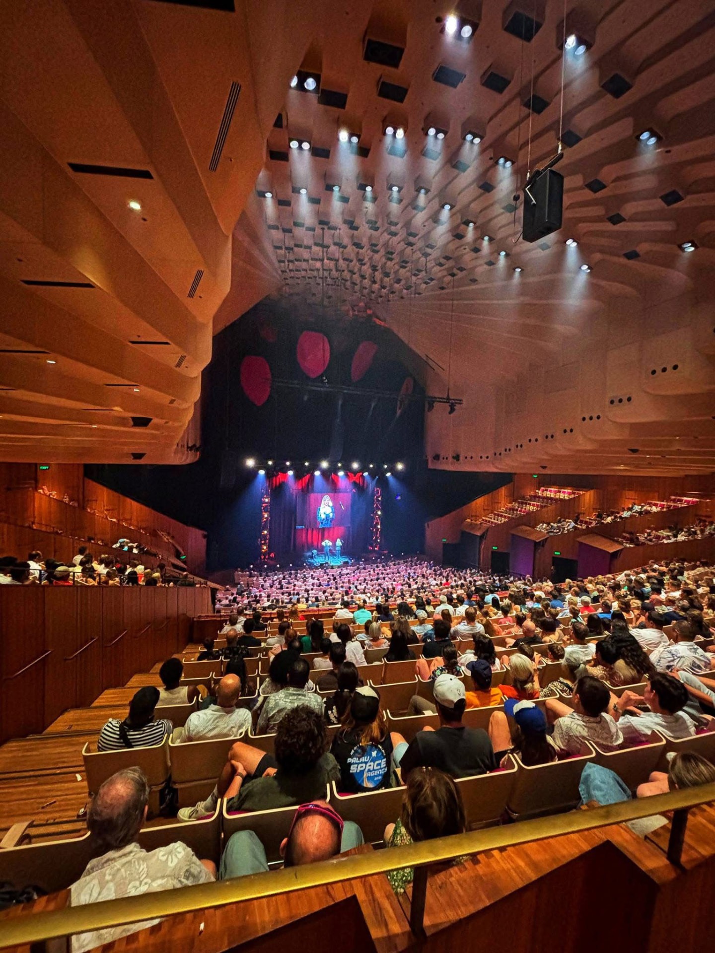 A full concert hall beneath a wooden ceiling watching the stage