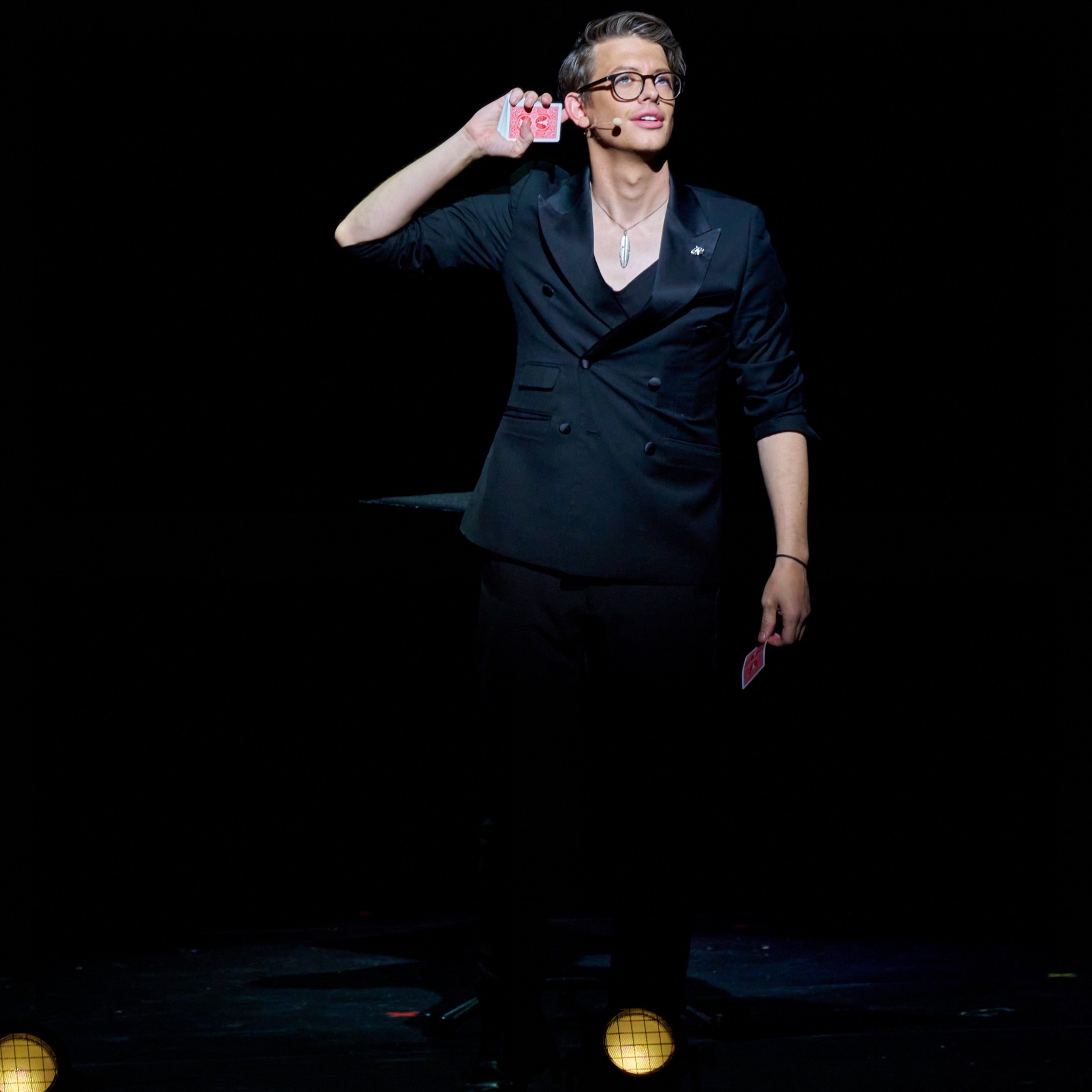 Matthew Pomeroy holding playing cards aloft on a darkened stage