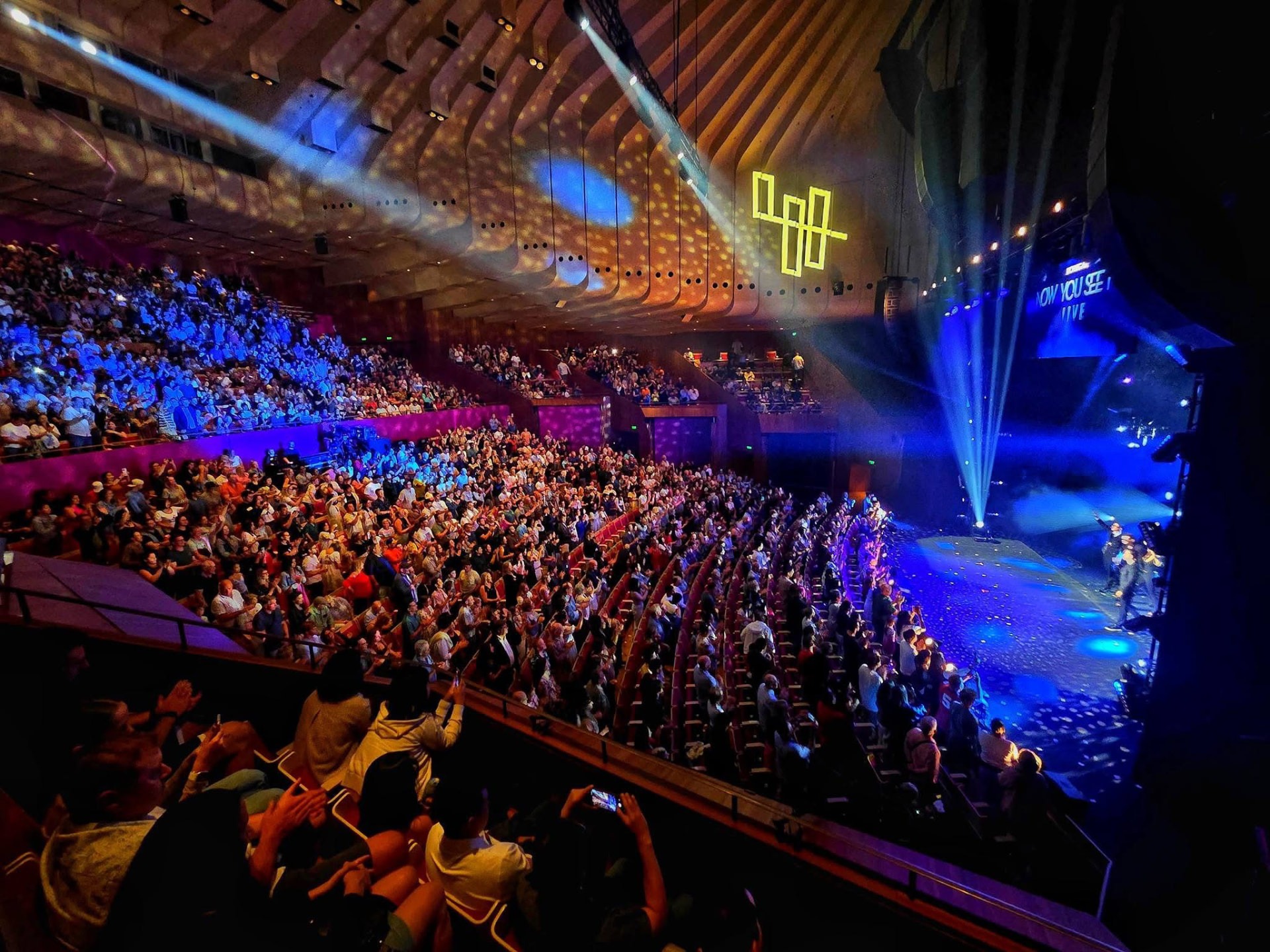 A tiered auditorium lit by blue beams during a performance
