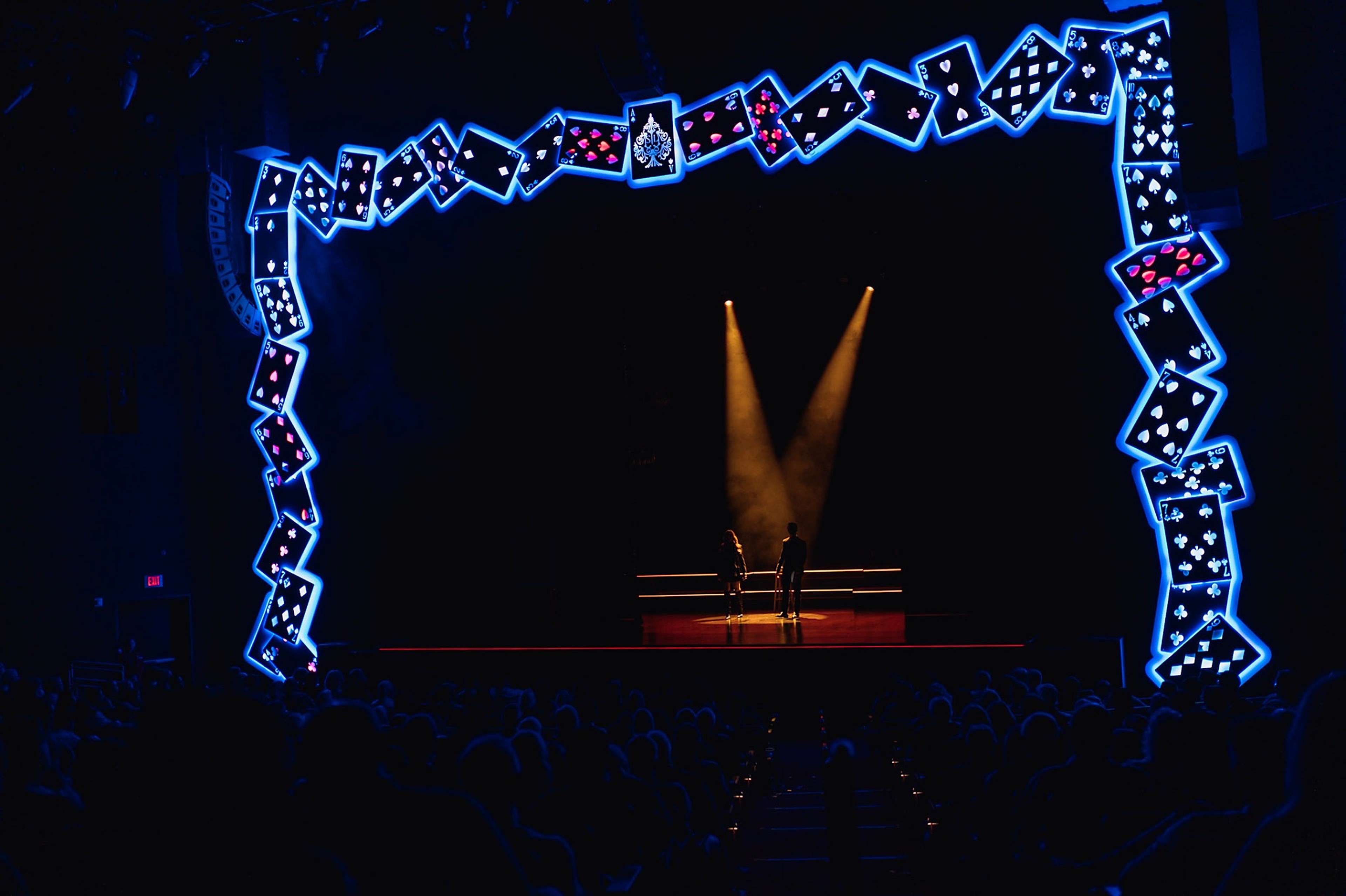 The Conjurors on stage beneath a giant arch of glowing playing cards