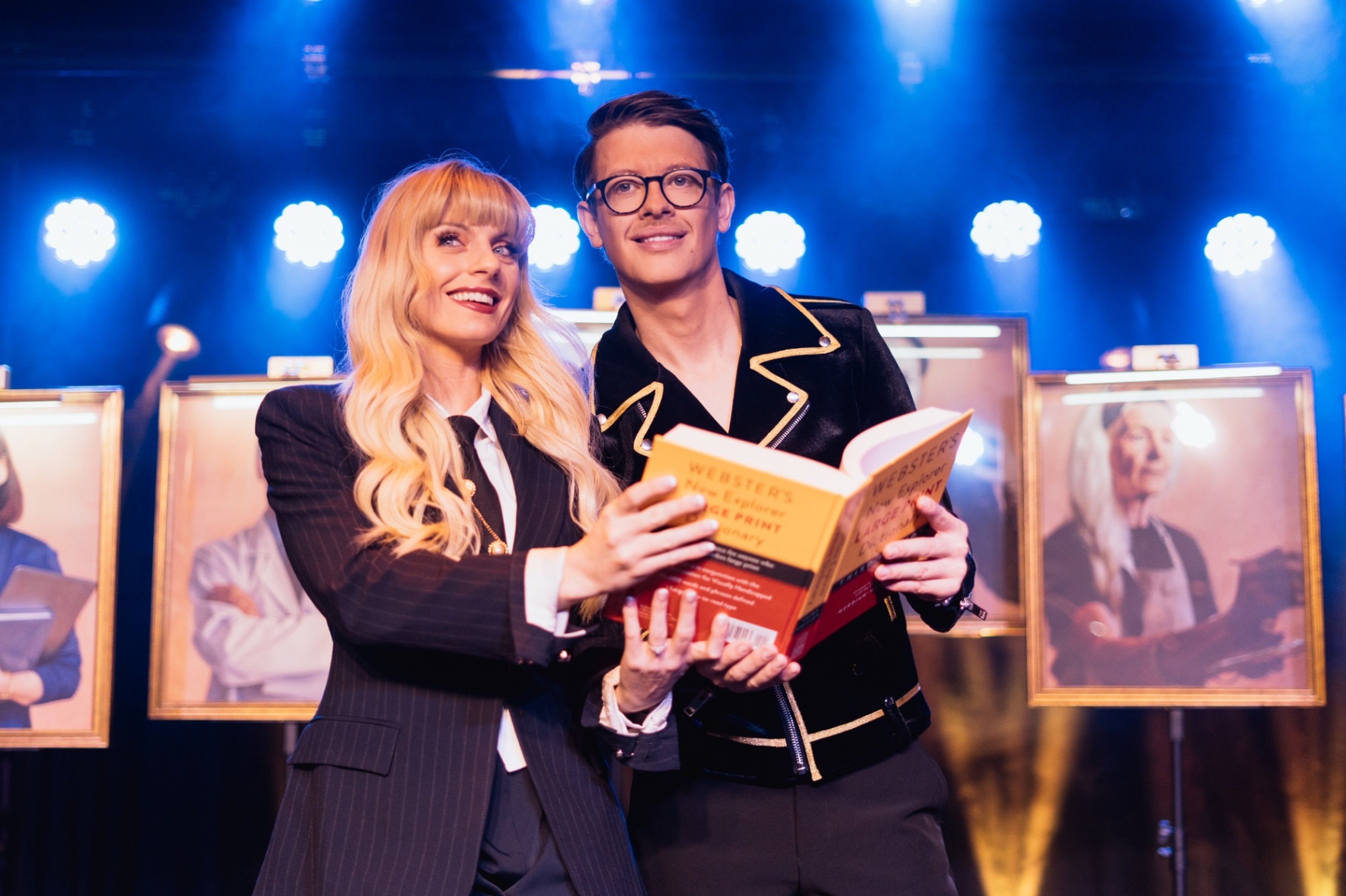 The Conjurors reading a dictionary together on a blue-lit stage