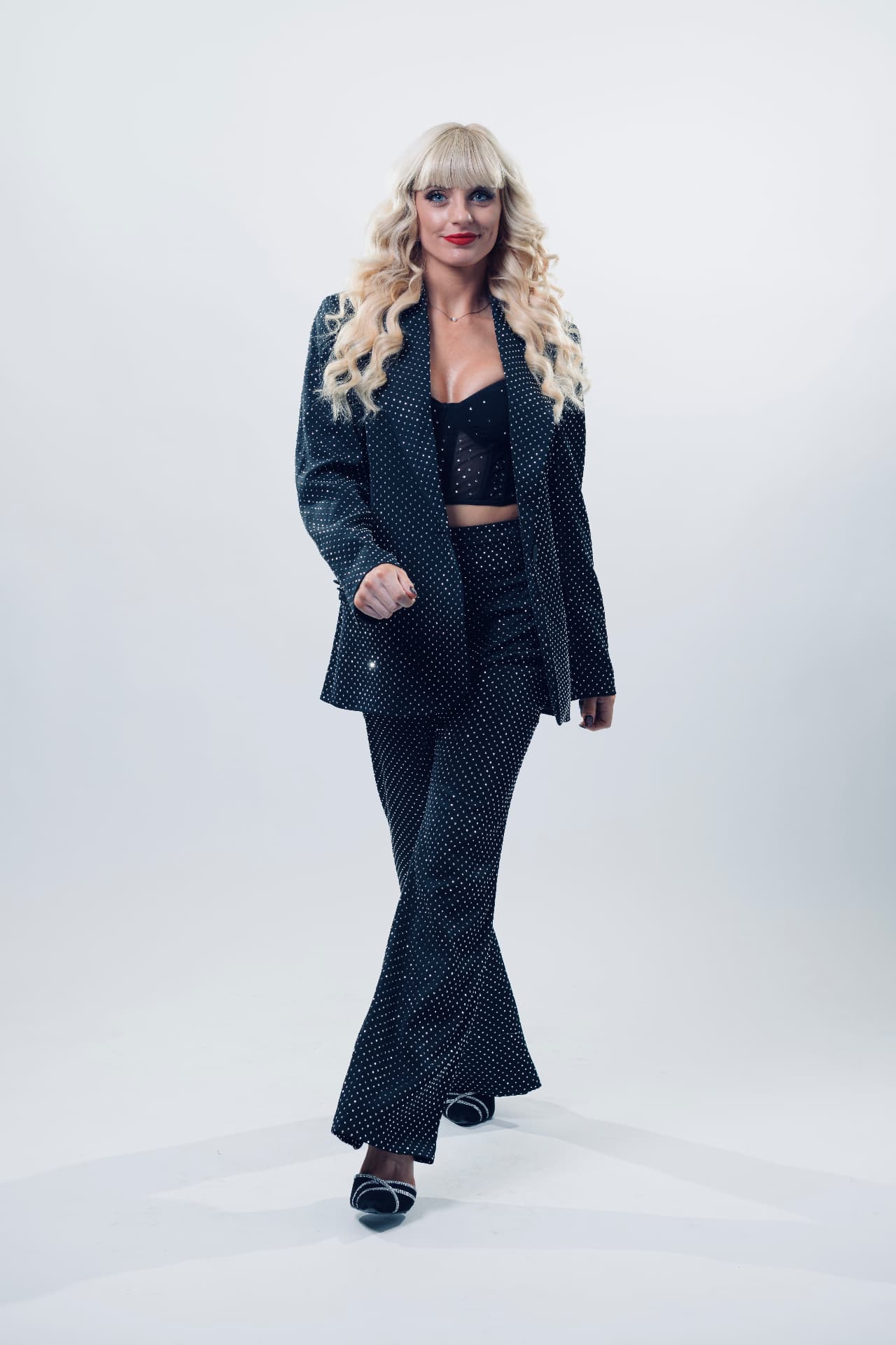 Natasha Lamb walking towards the camera in a black rhinestone trouser suit, studio photograph