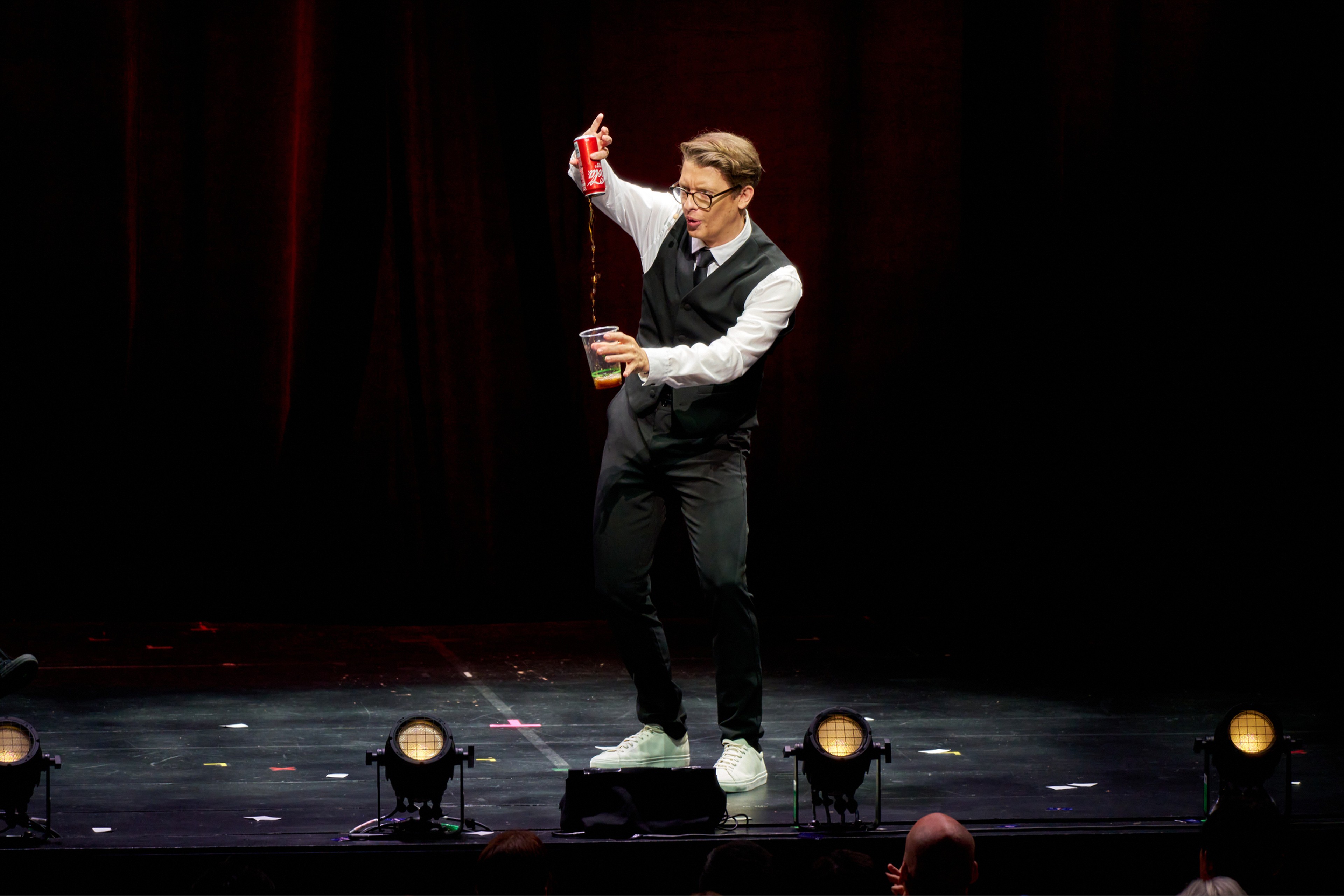 Matthew Pomeroy pouring a drink on stage before a red curtain