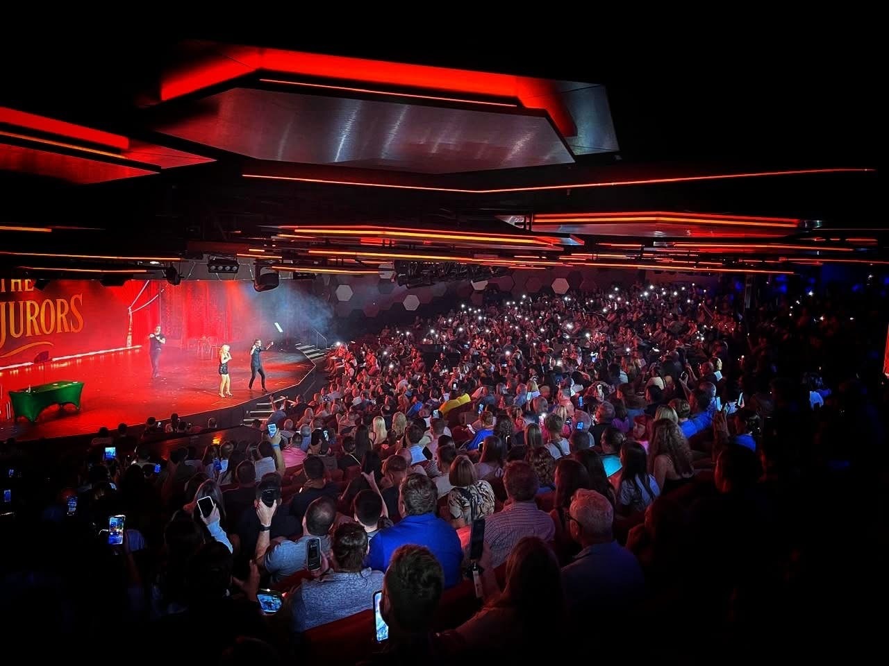 A packed theatre facing The Conjurors on a red-lit stage