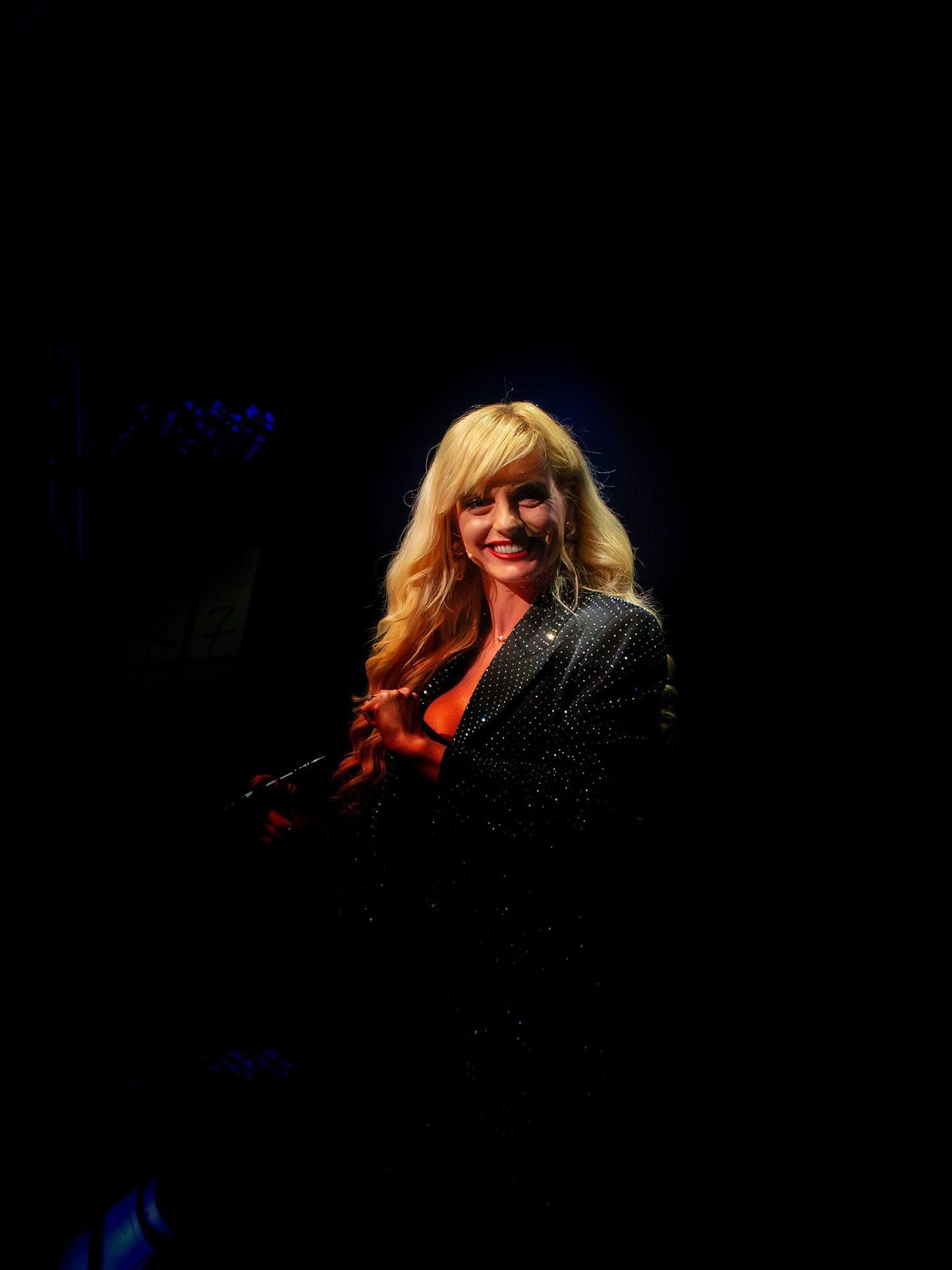 Natasha Lamb smiling in a single spotlight on a darkened stage