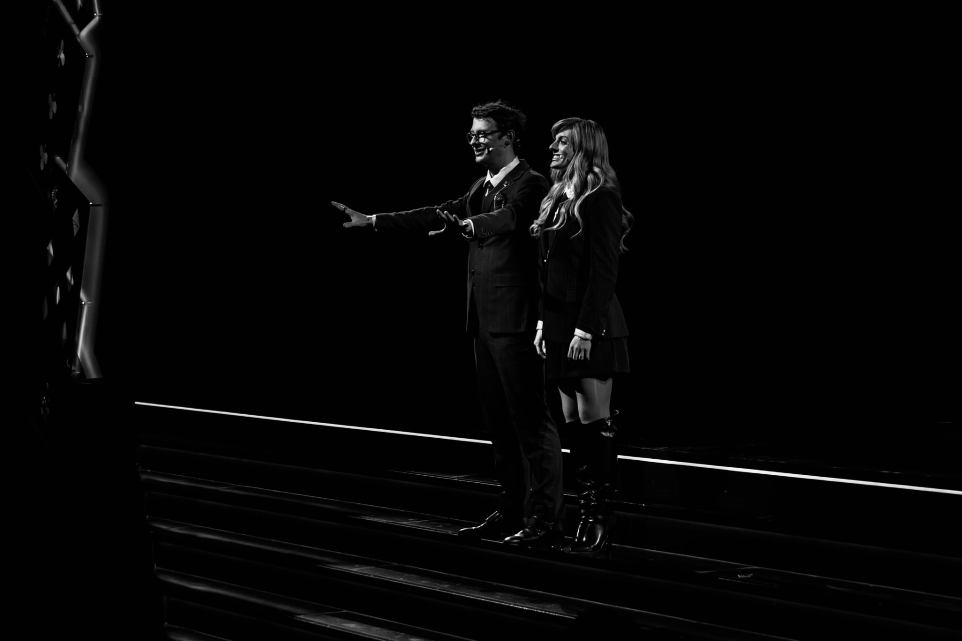 Matthew Pomeroy and Natasha Lamb standing on lit stage steps with their arms open in welcome