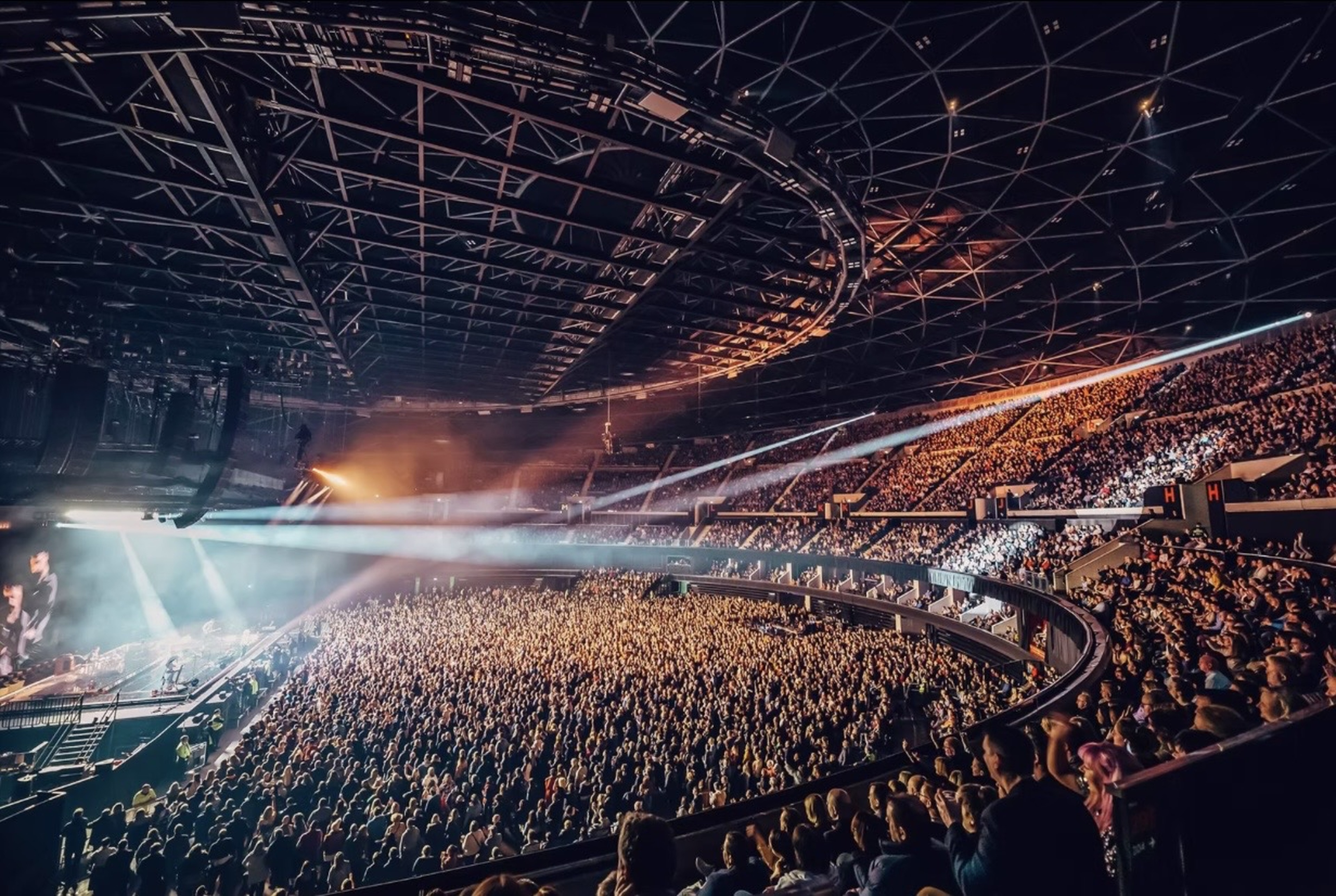 A panoramic view across a packed arena towards a brightly lit stage