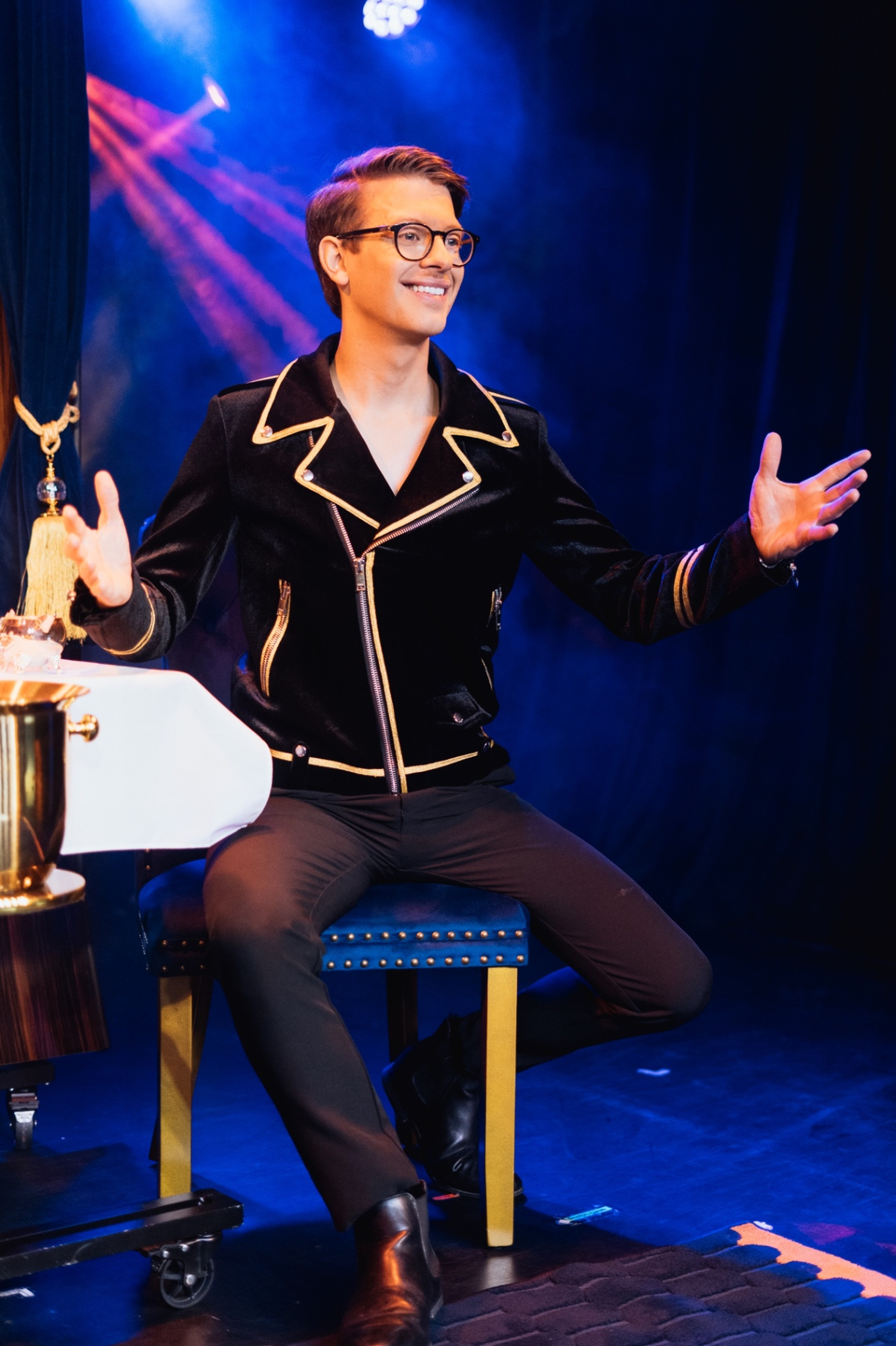 Matthew Pomeroy seated on stage under deep blue light, arms open