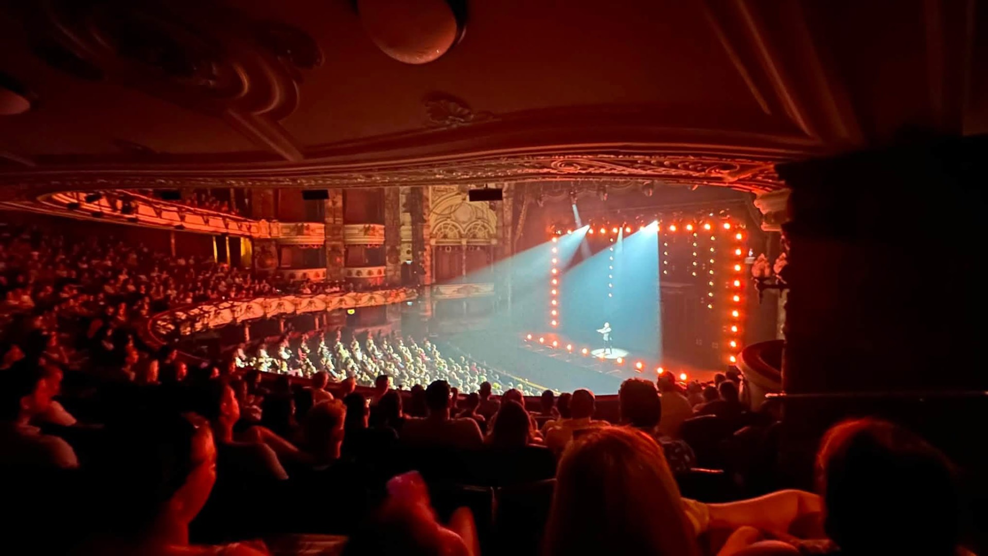 A grand auditorium in red light looking towards the lit stage