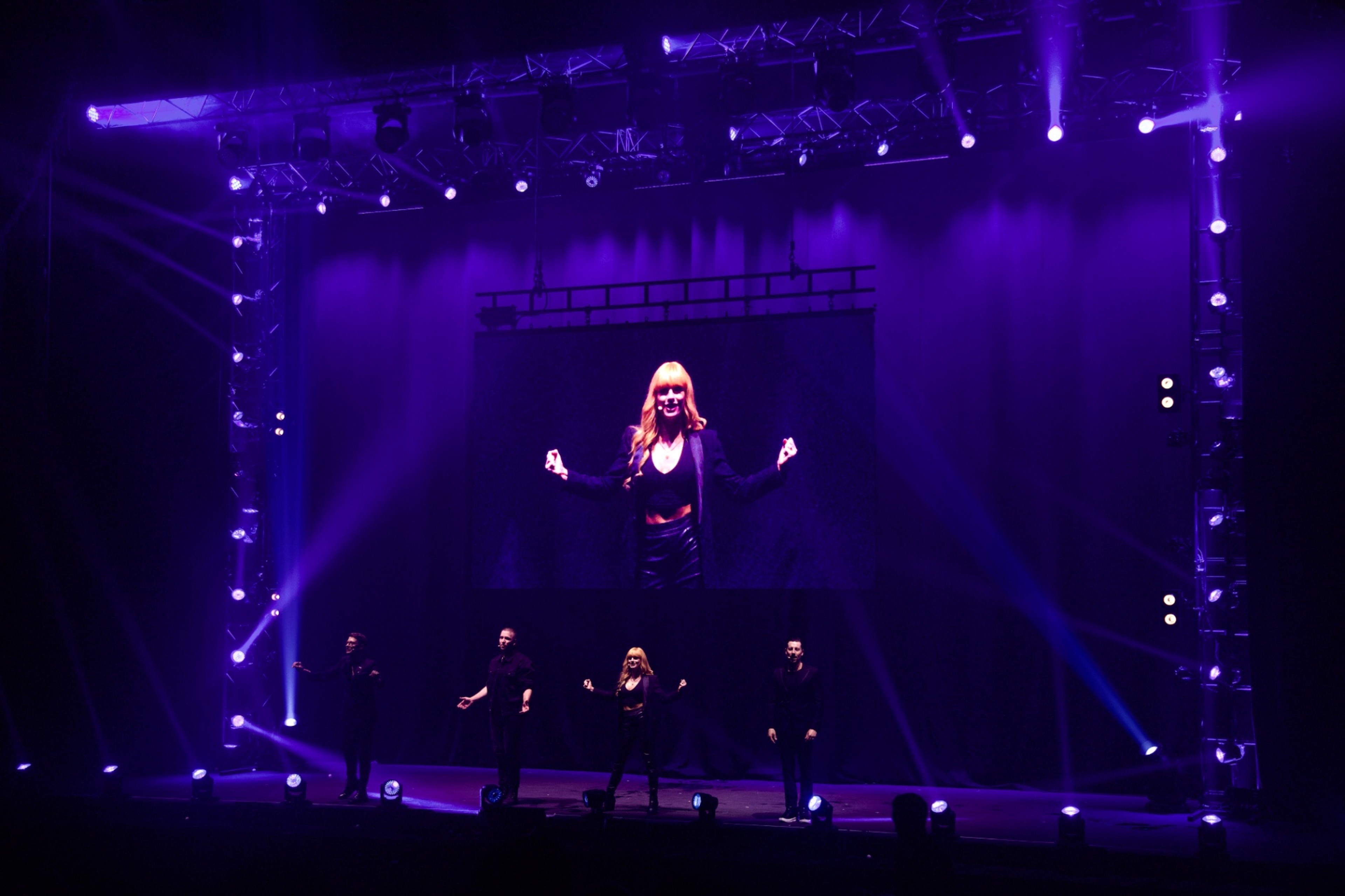 Natasha Lamb on the arena's big screen above a purple-lit stage
